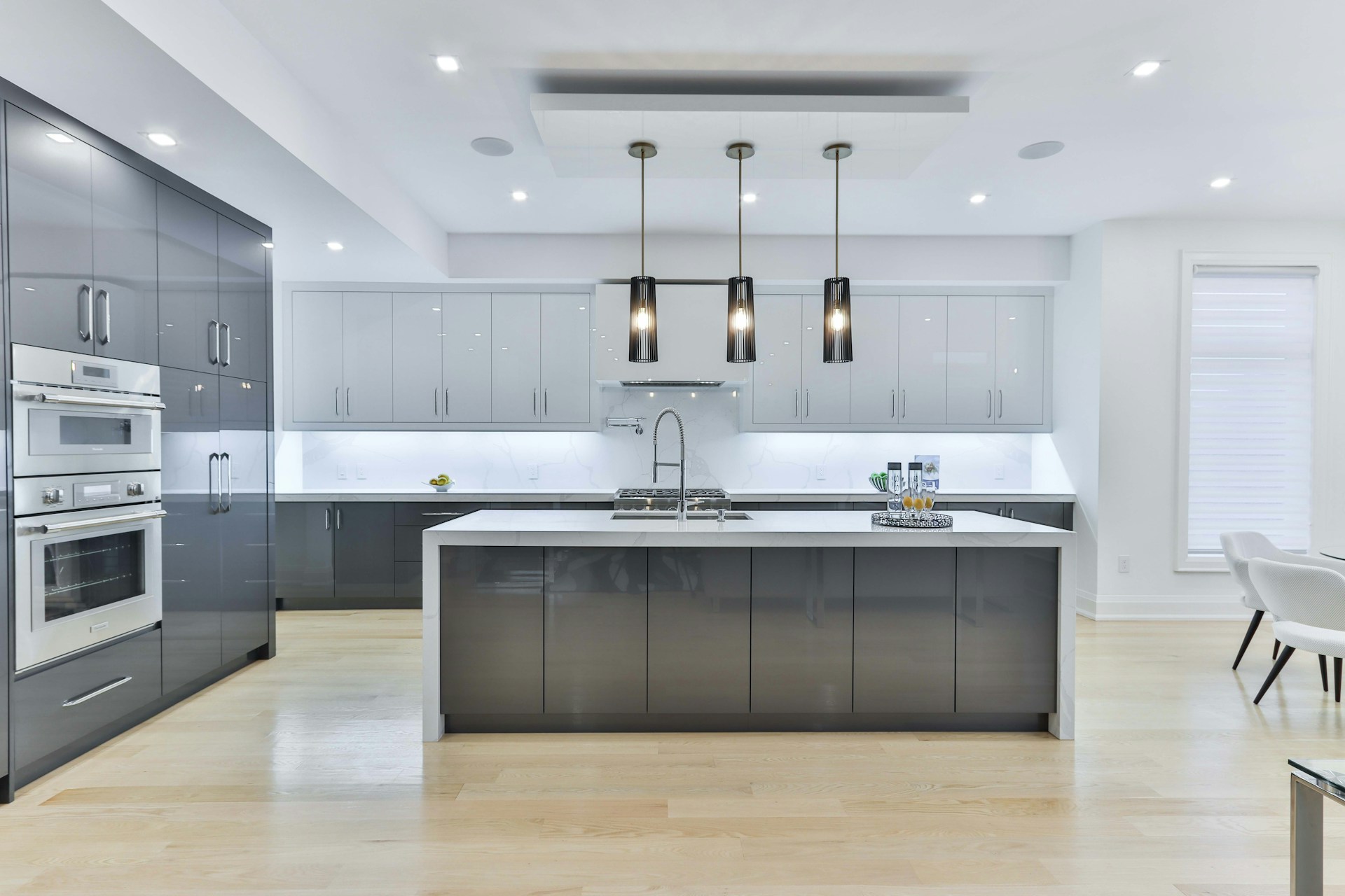Modern open-plan kitchen installation featuring grey handleless cabinets, white quartz waterfall island, integrated stainless steel appliances, pendant lighting, and polished concrete floors demonstrating professional kitchen fitting quality